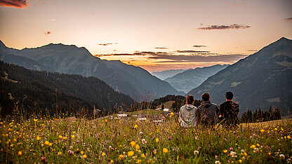 Sommerabend im Montafon beim Vermala Wirt mit Blumenwiese, Sonnenuntergang und Menschen mit Blick auf die Bergwelt.